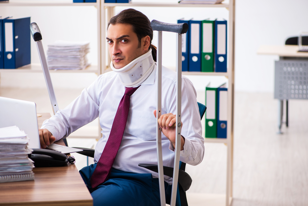 Common Types Of Pain & Suffering - Leg injured male employee with crutches at workplace